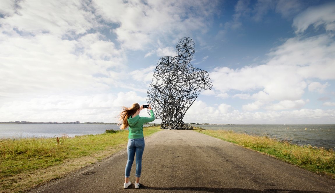 Lady takes photo of Land Art Flevoland Antony Gormley's Exposure (also called: the squatting man)